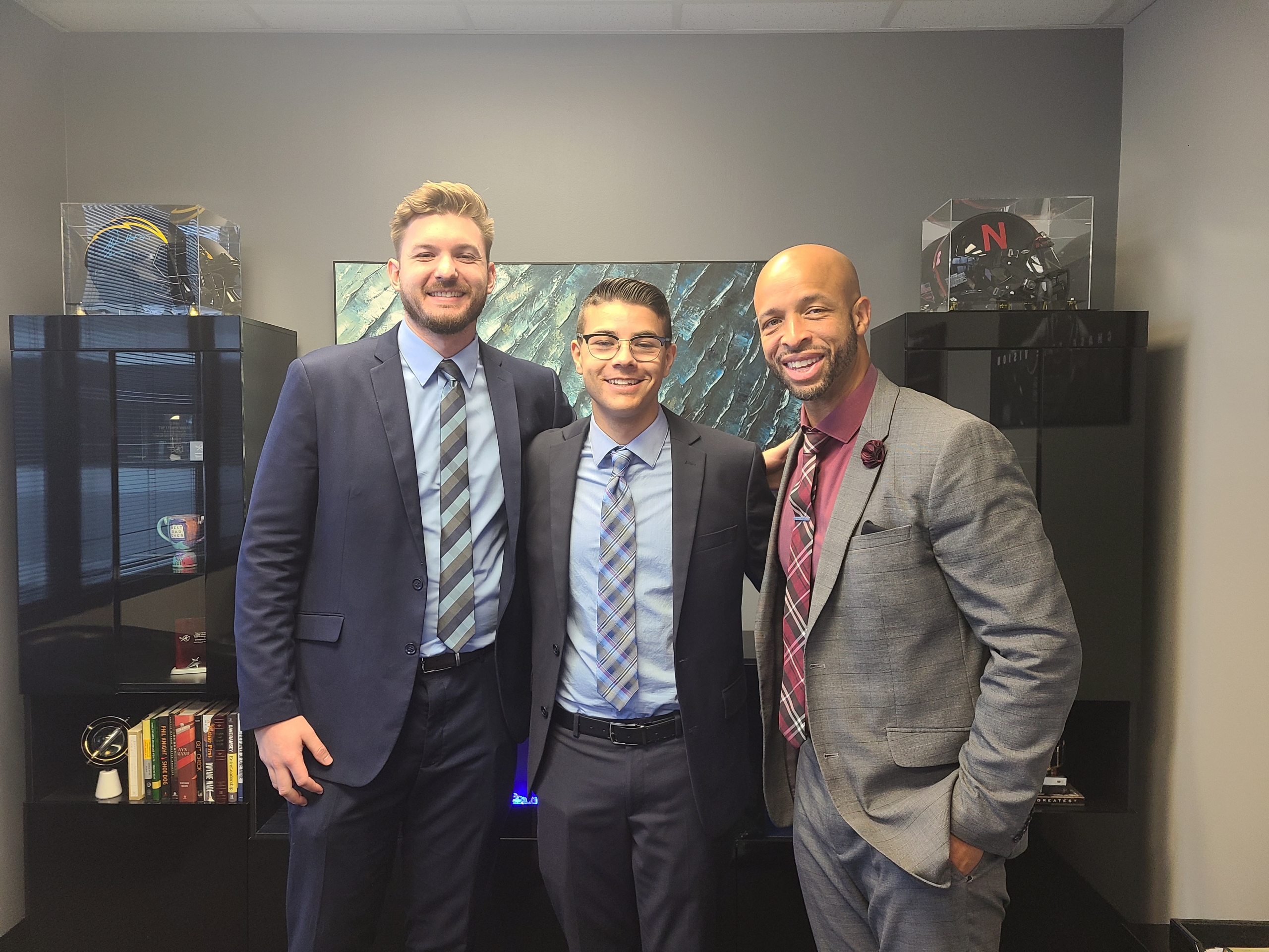 Three True Vision team members in an office with sports memorabilia, celebrating company culture