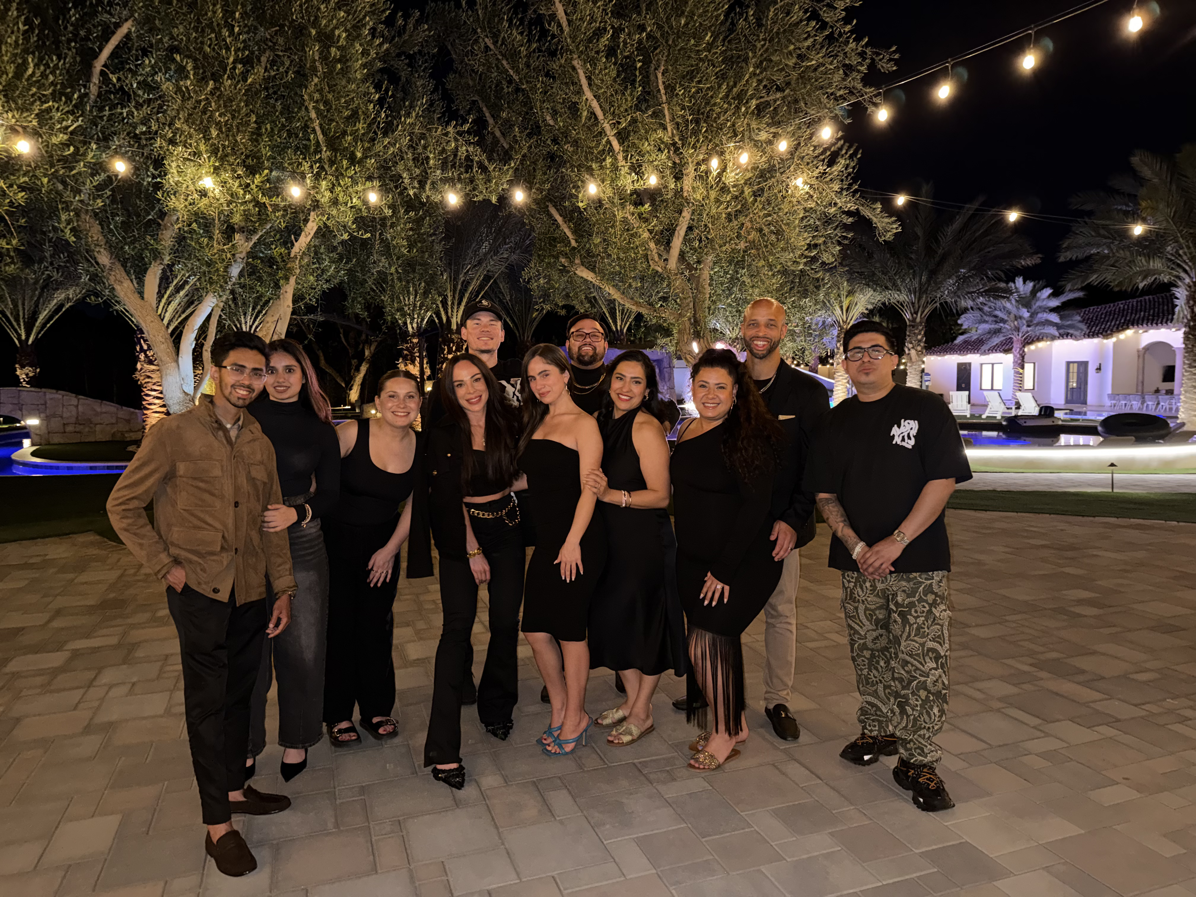 Large True Vision team group photo at an outdoor evening event with string lights